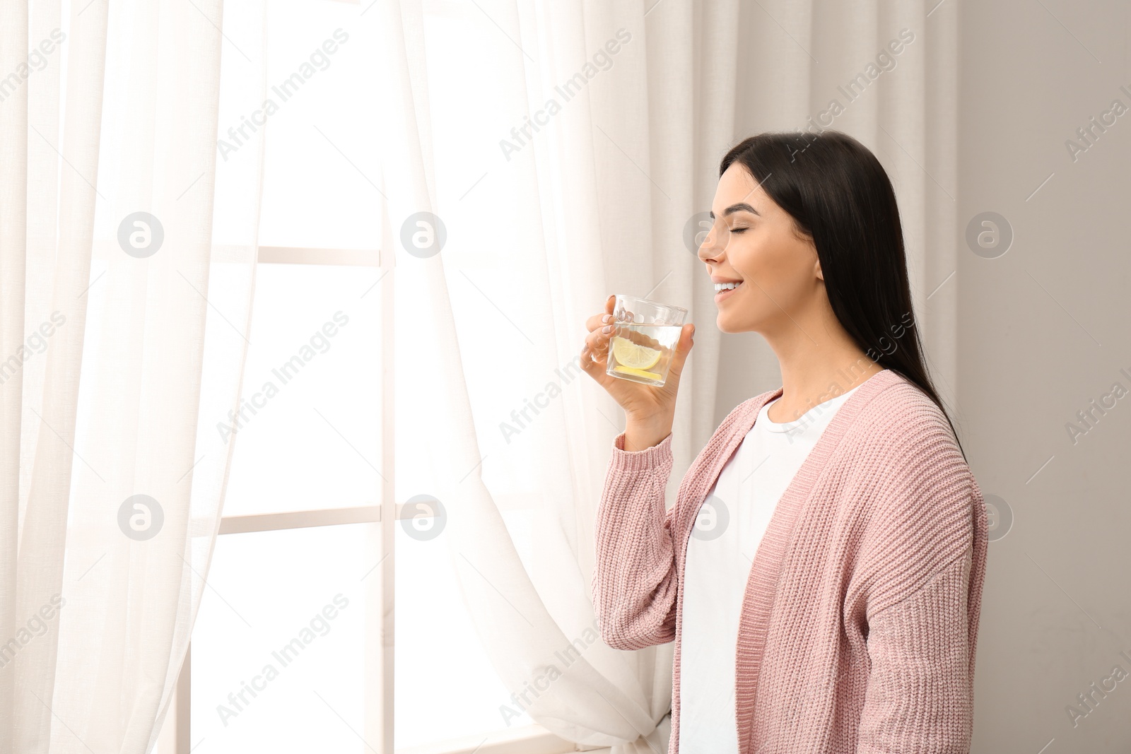 Photo of Beautiful young woman drinking fresh lemon water indoors. Space for text