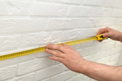 Photo of Man measuring brick wall indoors, closeup. Construction tool