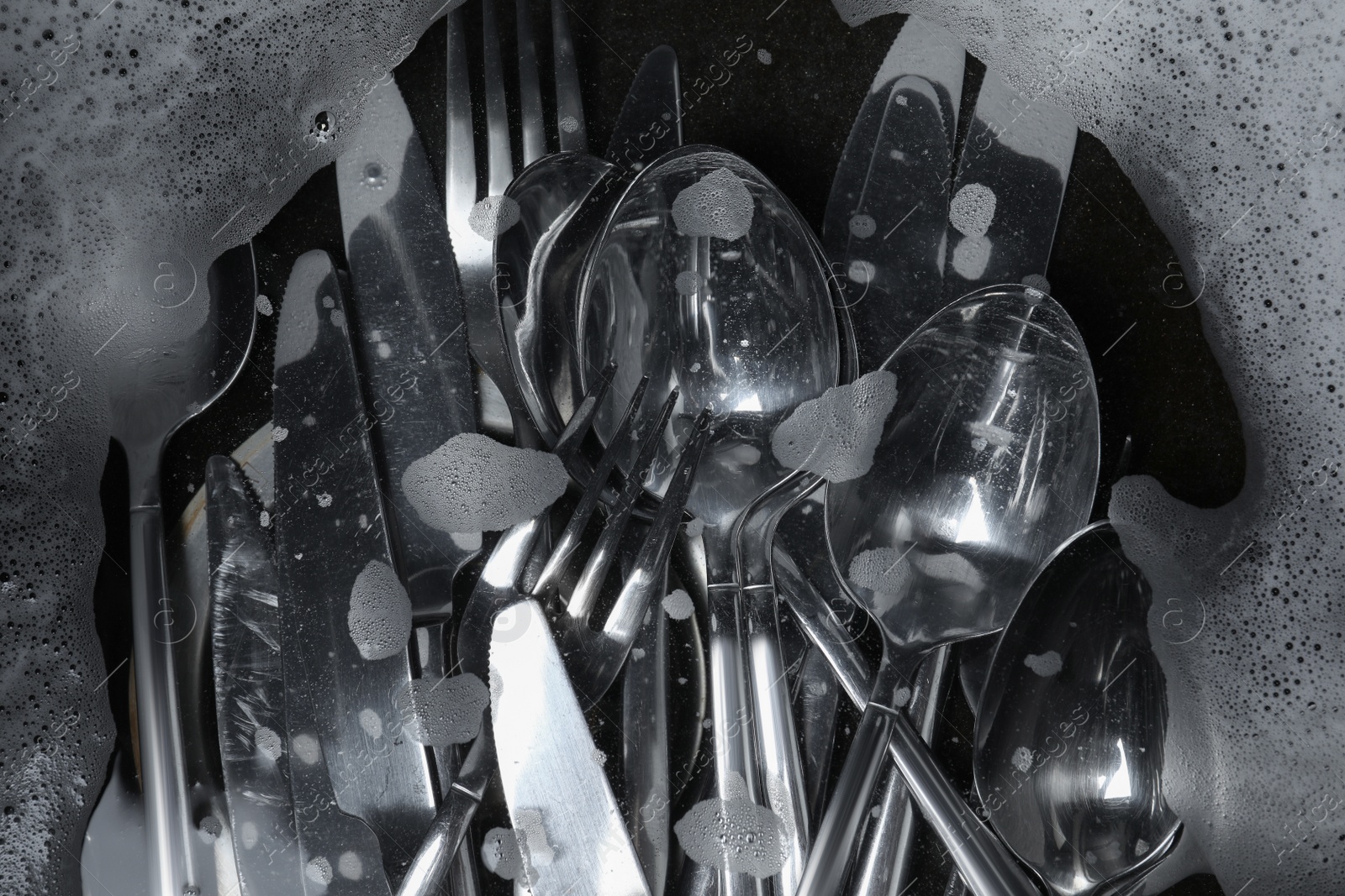 Photo of Washing silver spoons, forks and knives in water with foam, flat lay