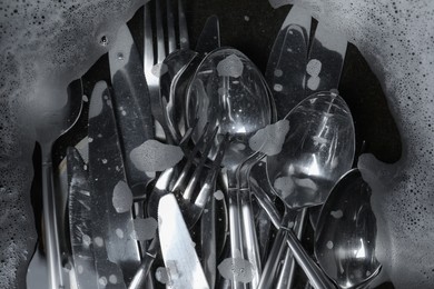 Photo of Washing silver spoons, forks and knives in water with foam, flat lay