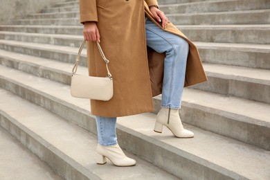 Stylish woman with trendy beige bag on stairs outdoors, closeup