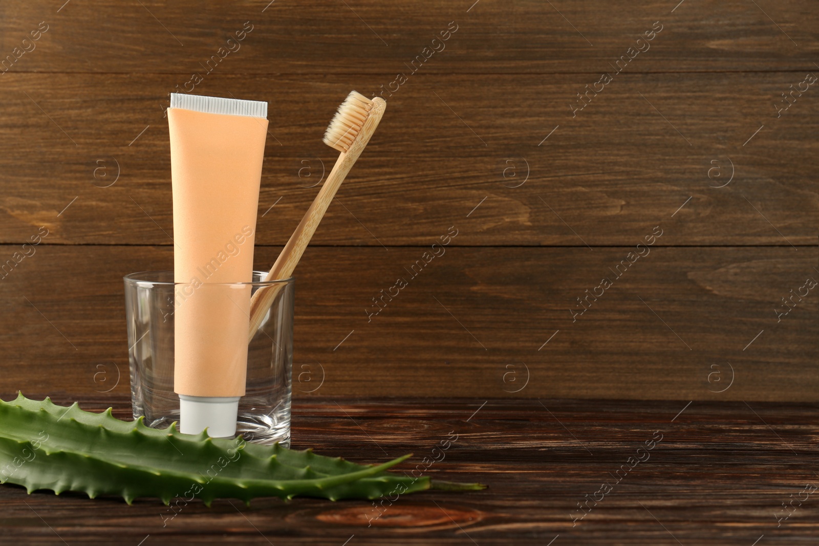 Photo of Aloe vera toothpaste in blank tube, brush and green leaves on wooden table, space for text