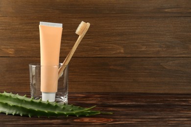 Aloe vera toothpaste in blank tube, brush and green leaves on wooden table, space for text