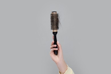 Photo of Woman holding brush with lost hair on grey background, closeup. Alopecia problem