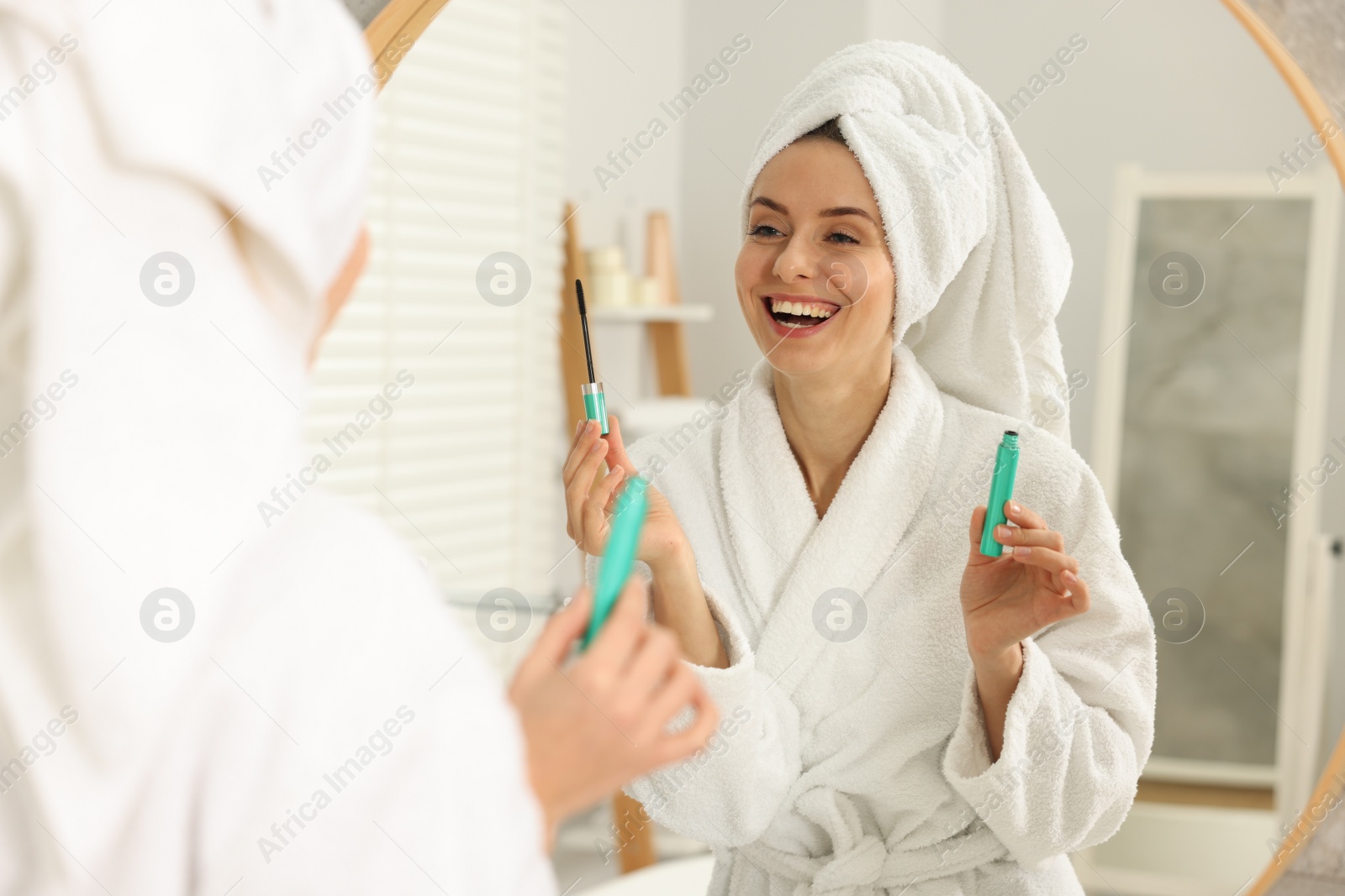 Photo of Beautiful woman with mascara near mirror in bathroom
