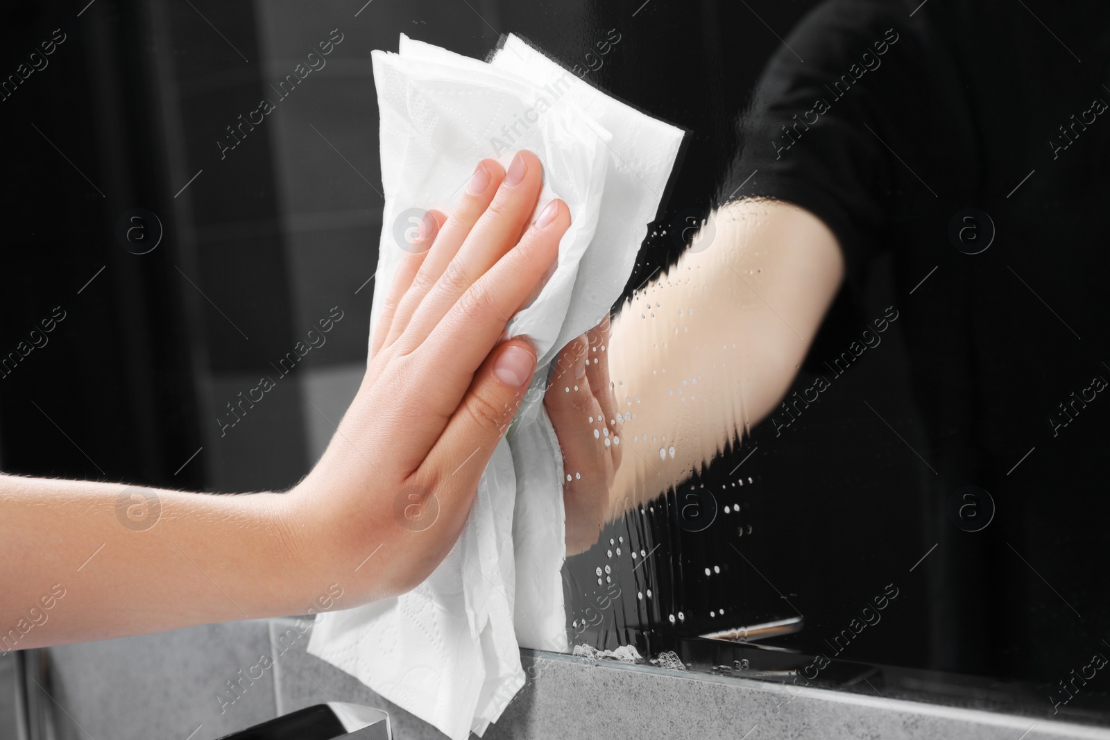 Photo of Woman cleaning mirror with paper towel in bathroom, closeup