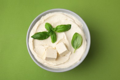 Photo of Delicious tofu sauce and basil leaves on green background, top view