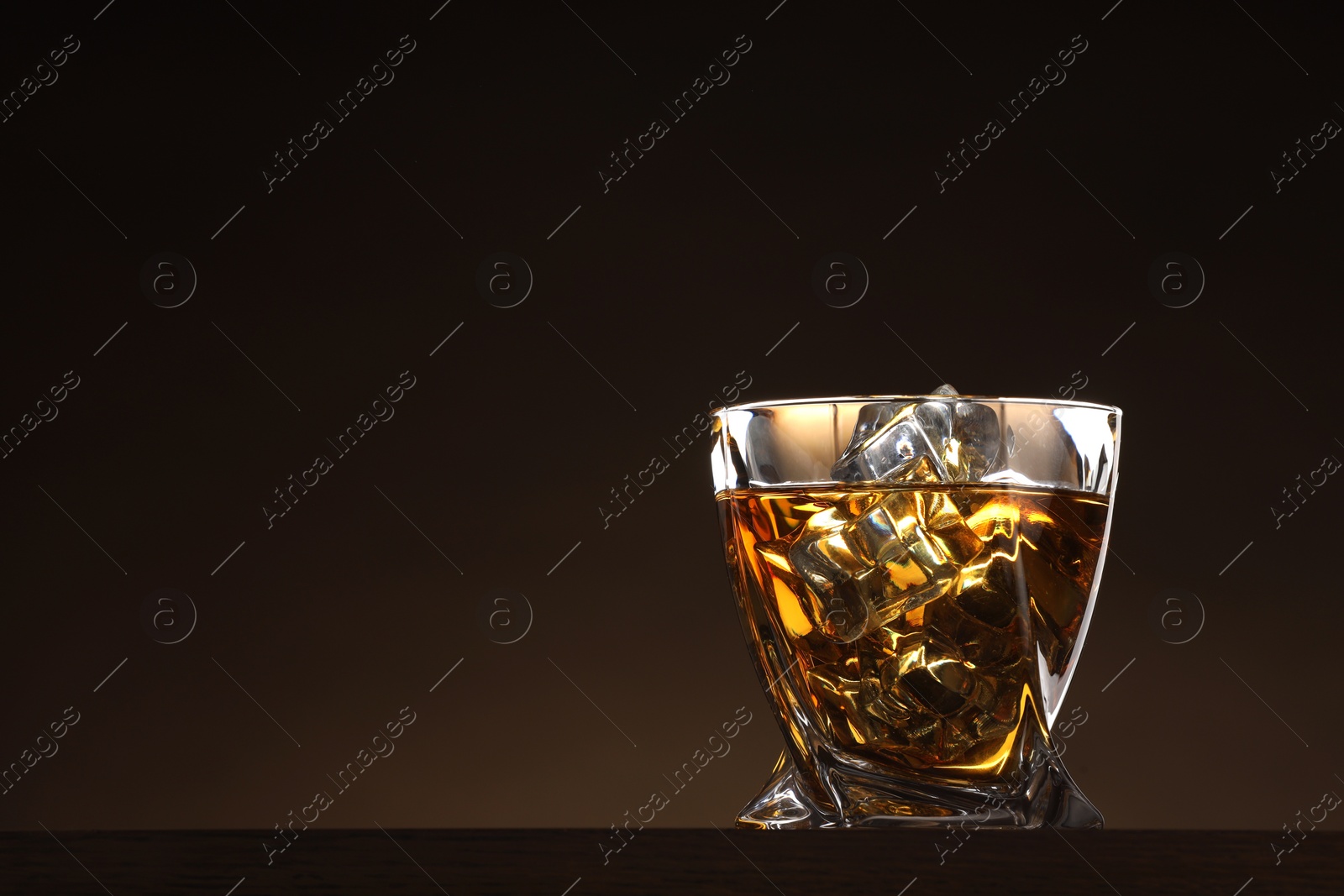 Photo of Whiskey with ice cubes in glass on table against brown background. Space for text
