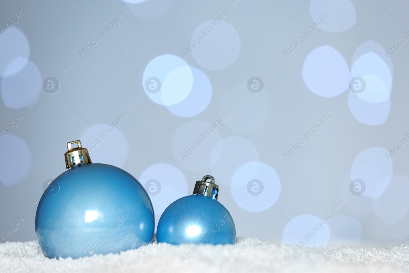 Photo of Beautiful light blue Christmas balls on snow against blurred festive lights. Space for text