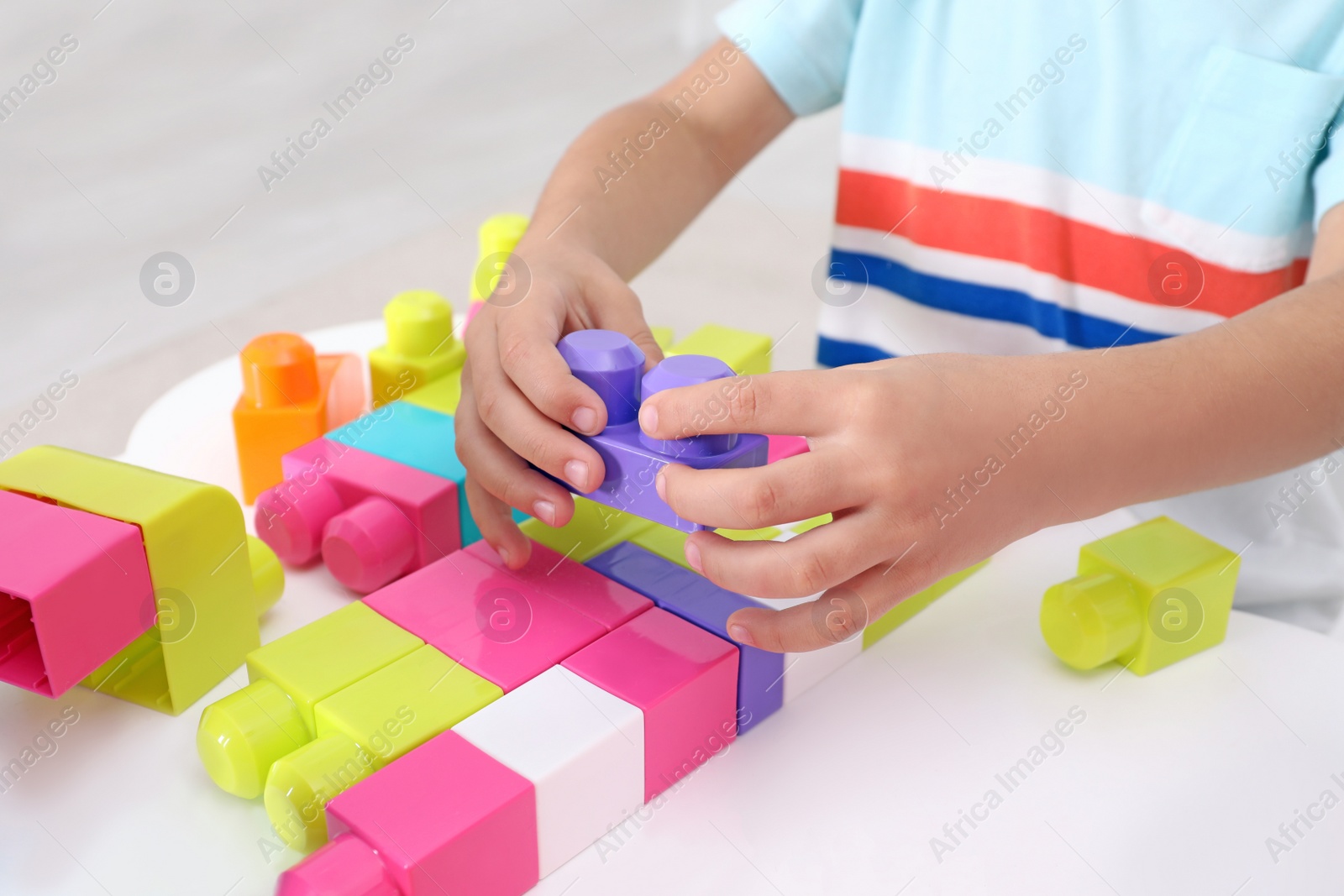 Photo of Little child playing with colorful building blocks at table indoors, closeup