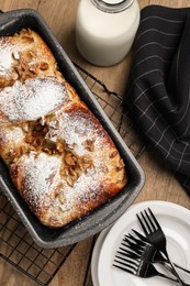 Delicious yeast dough cake in baking pan and milk on wooden table, flat lay