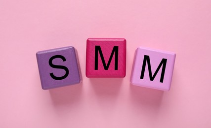 Photo of Colorful cubes with abbreviation SMM (Social media marketing) on pink background, flat lay