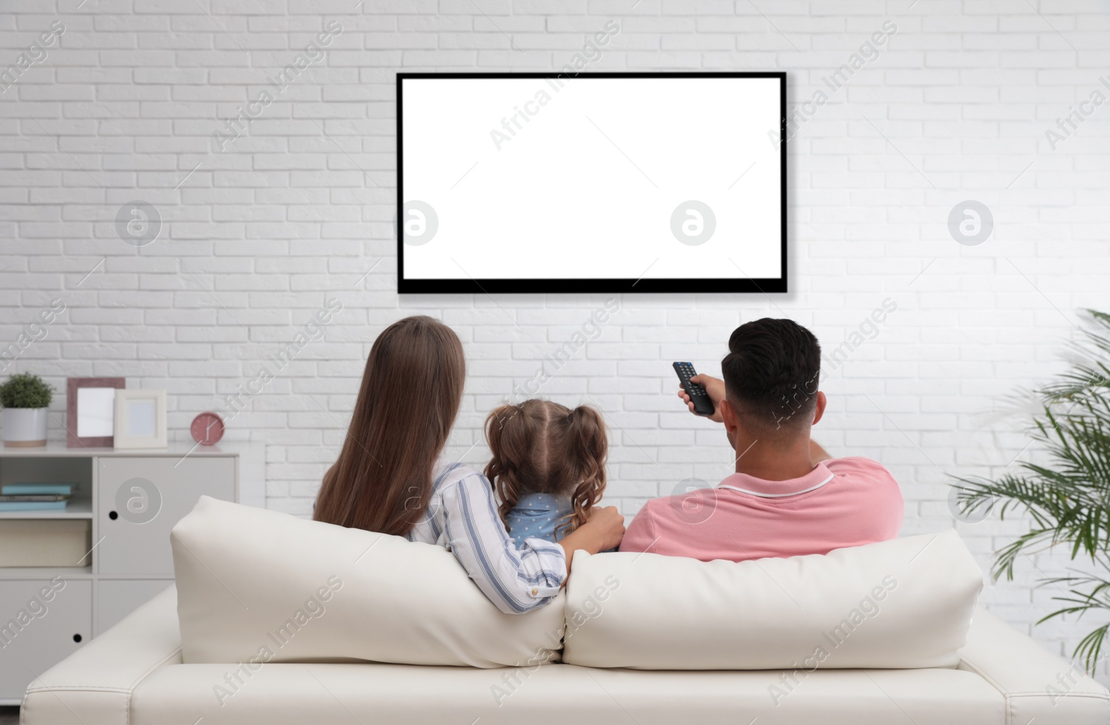 Photo of Family watching TV on sofa at home, back view