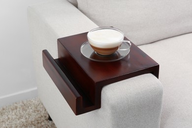 Photo of Cup of coffee on sofa with wooden armrest table indoors. Interior element