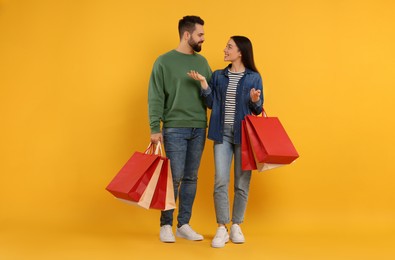 Photo of Happy couple with shopping bags discussing on orange background