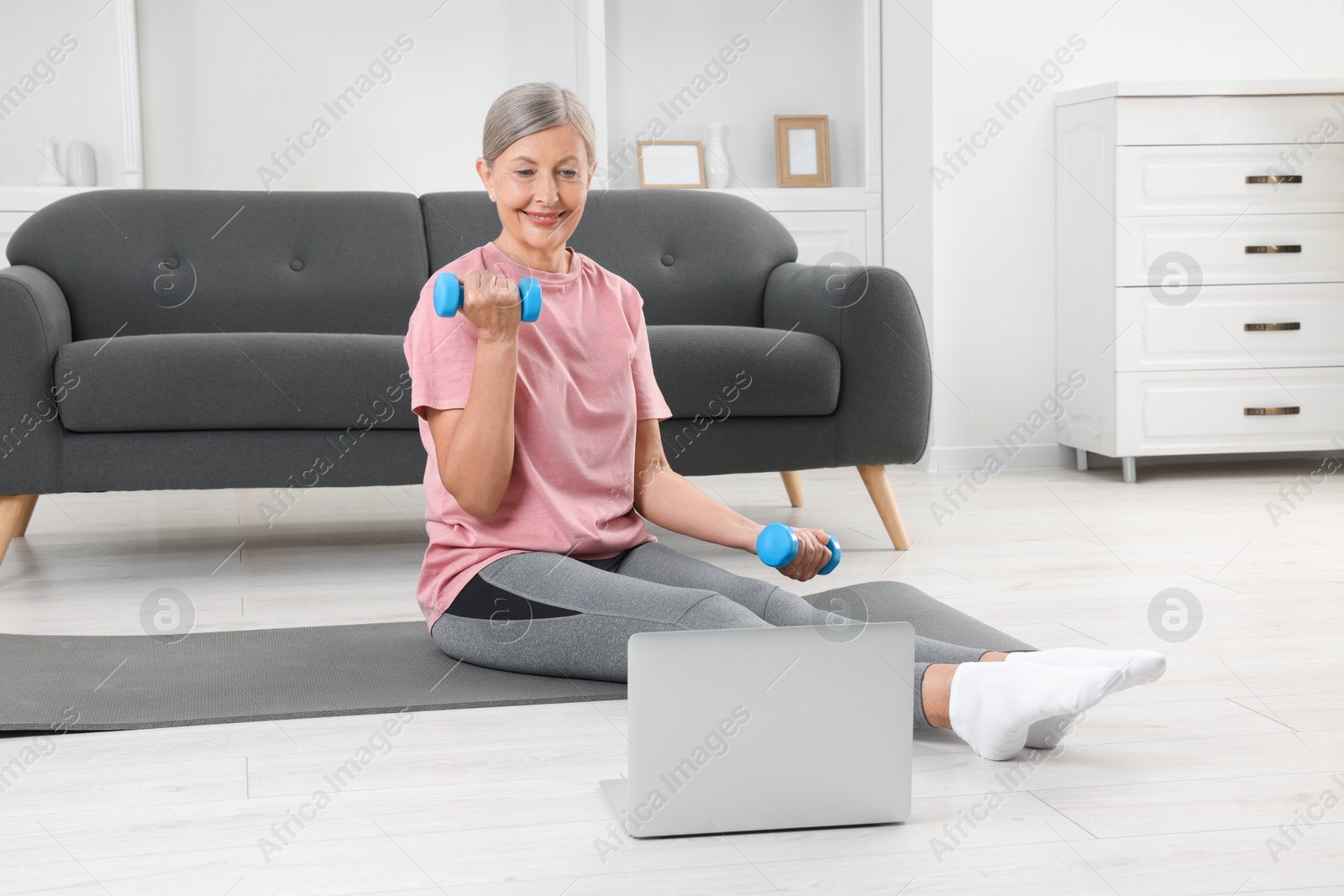 Photo of Senior woman exercising with dumbbells while watching online tutorial at home. Sports equipment