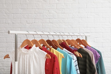 Wardrobe rack with stylish clothes near brick wall indoors