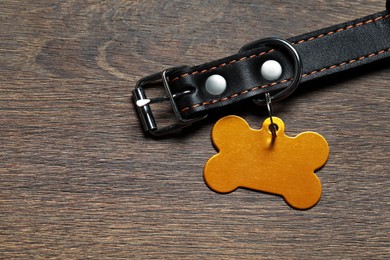 Photo of Leather dog collar with yellow tag in shape of bone on wooden table, flat lay. Space for text