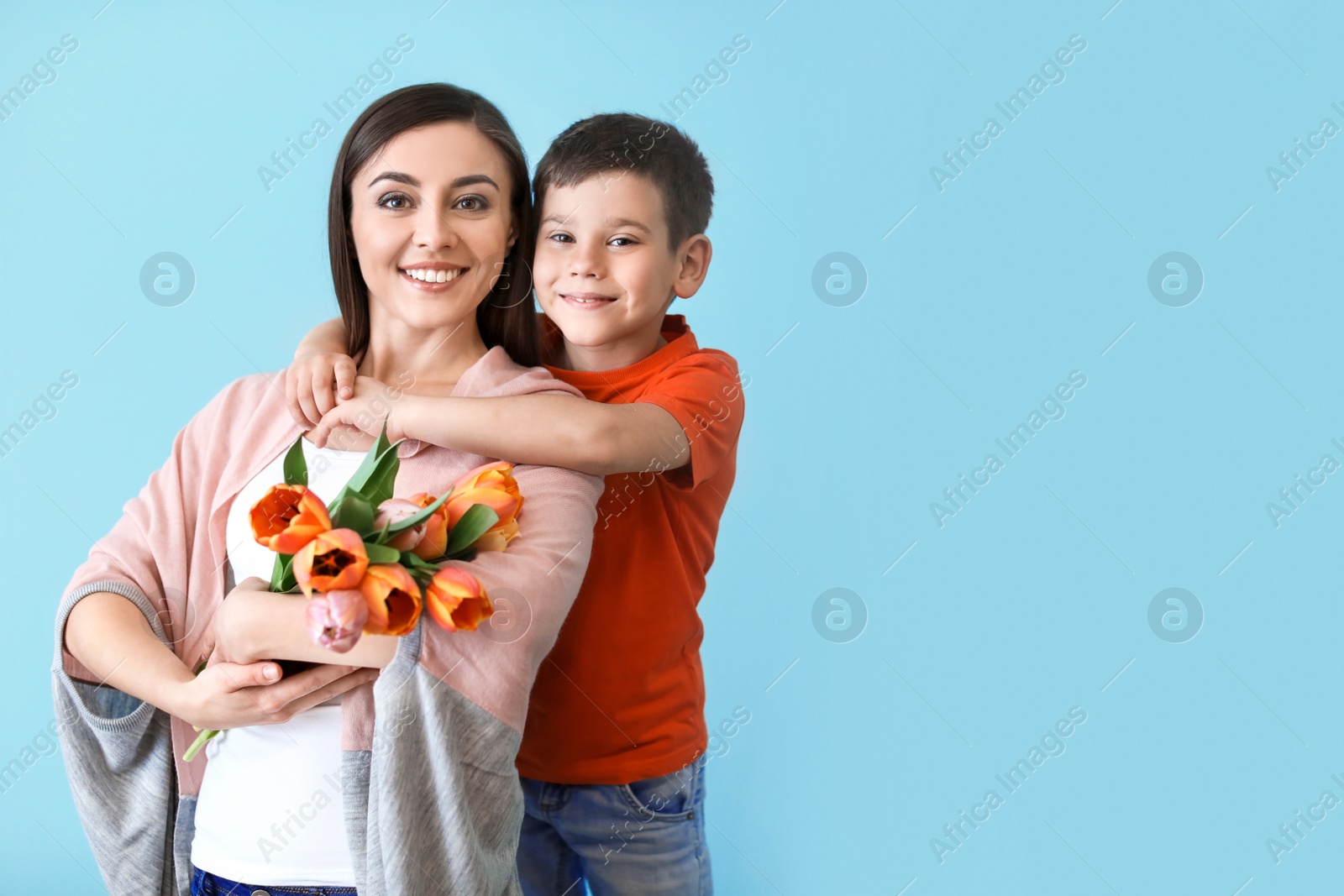 Photo of Portrait of happy woman with flowers and her son on color background. Mother's day celebration