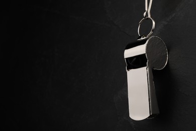 Photo of Referee equipment. Metal whistle on black textured background, closeup and space for text