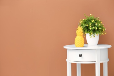 Stylish pineapple candle and houseplant on table against color background