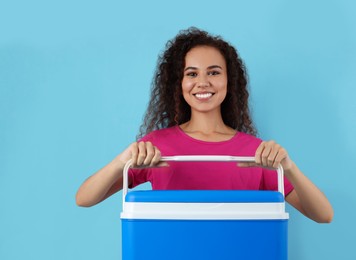 Photo of Happy young African American woman with cool box on light blue background