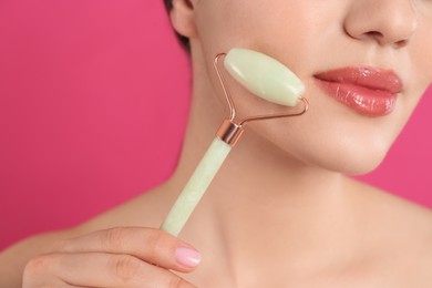 Photo of Woman using natural jade face roller on pink background, closeup