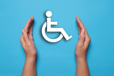 Image of Disability inclusion. Woman protecting wheelchair symbol on light blue background, closeup