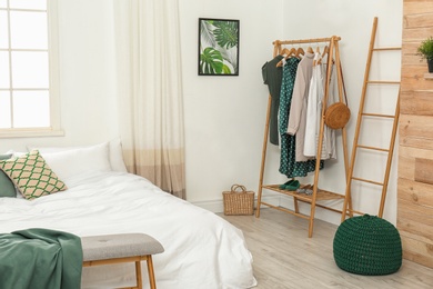 Photo of Wooden rack with clothes in modern bedroom interior