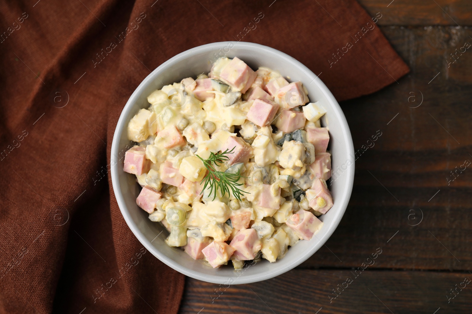 Photo of Tasty Olivier salad with boiled sausage in bowl on wooden table, top view