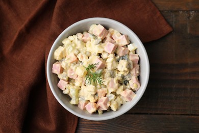Photo of Tasty Olivier salad with boiled sausage in bowl on wooden table, top view
