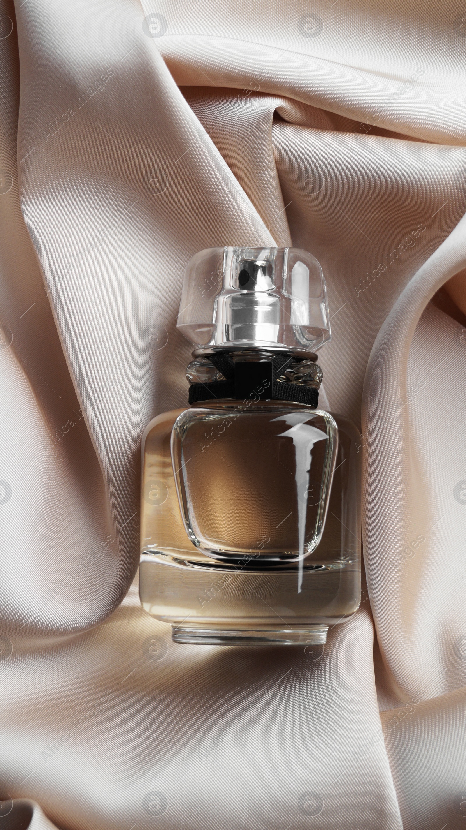 Photo of Luxury bottle of perfume on beige silk, top view