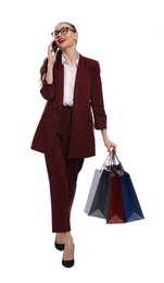 Stylish young woman with shopping bags talking on smartphone against white background