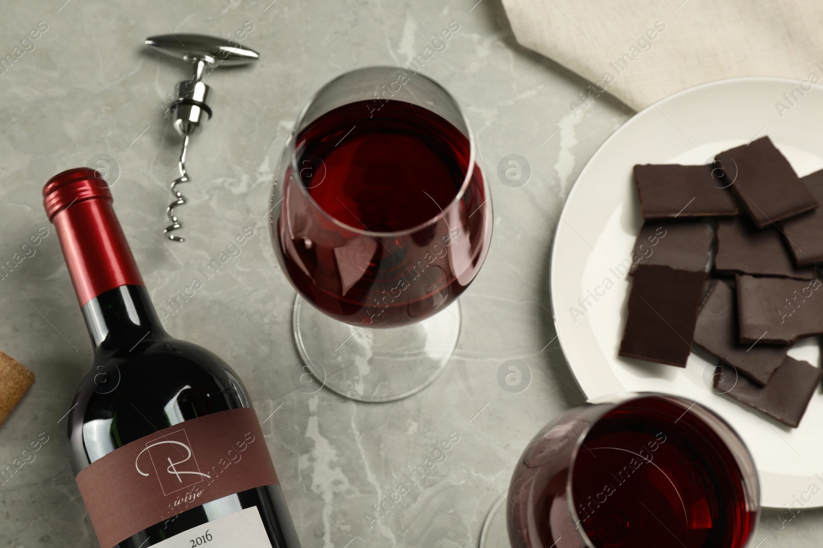 Photo of Glasses and bottle of red wine with chocolate on light marble table, above view