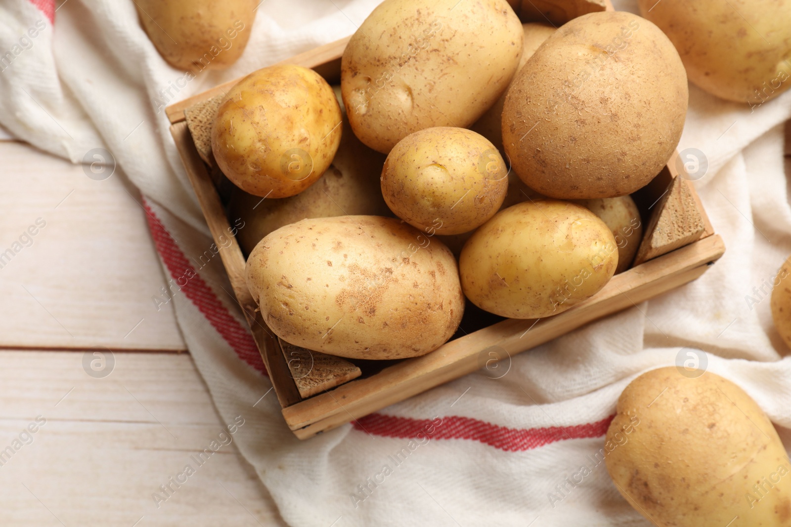 Photo of Raw fresh potatoes with crate on light wooden table, top view