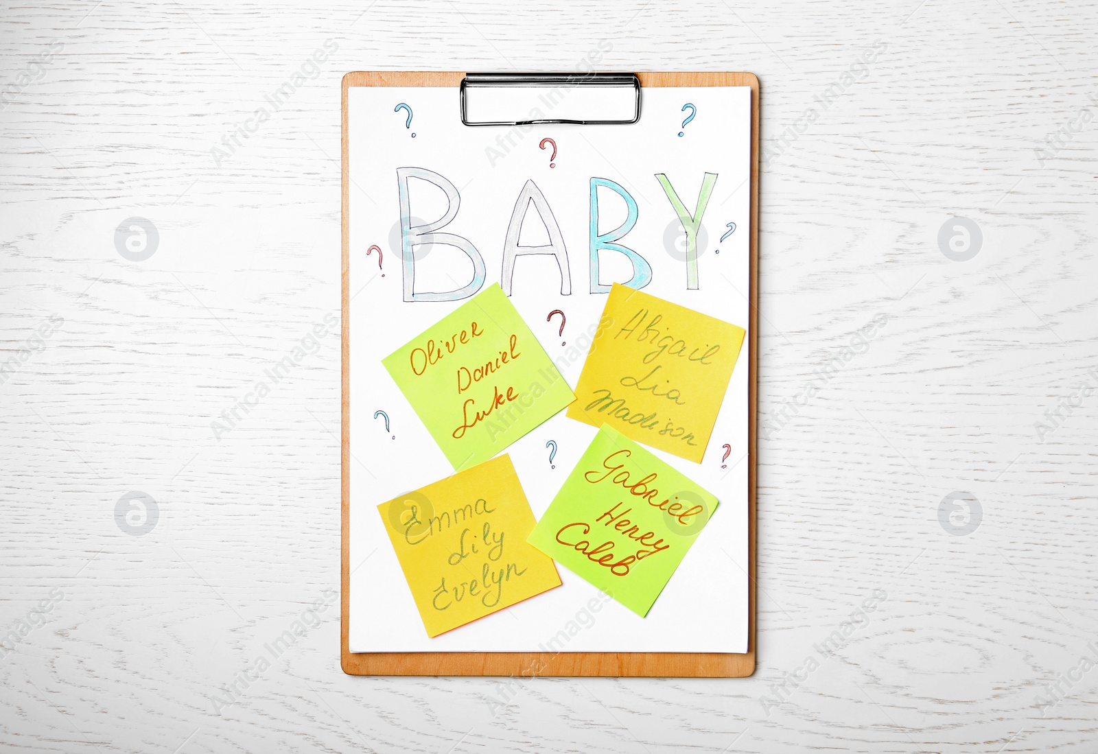 Photo of Clipboard with written different baby names on white wooden table, top view