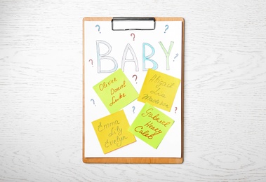 Clipboard with written different baby names on white wooden table, top view