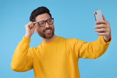 Photo of Smiling man taking selfie with smartphone on light blue background