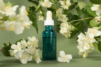 Photo of Essential oil in bottle and beautiful jasmine flowers on pale green background