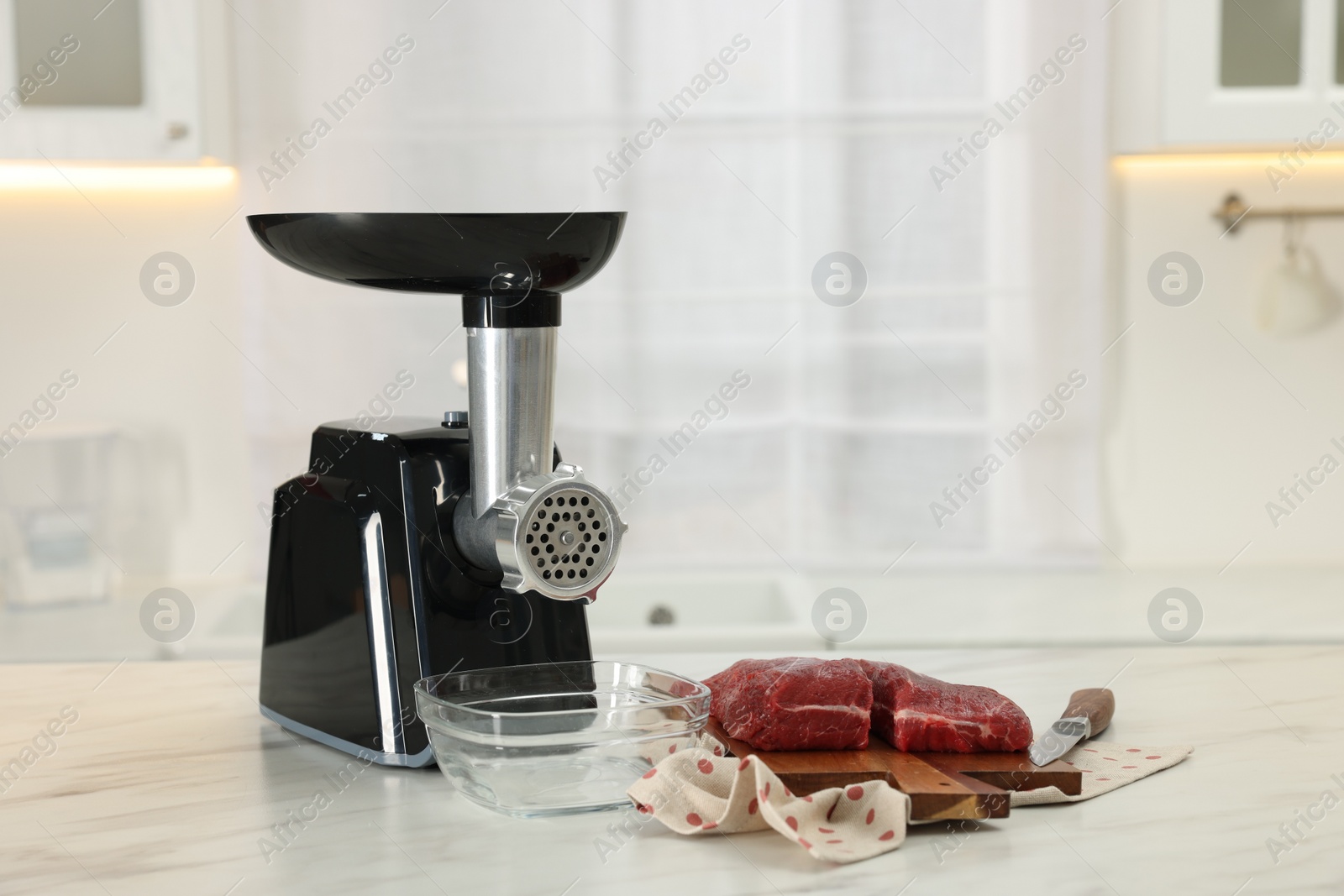 Photo of Electric meat grinder with beef and knife on white marble table in kitchen