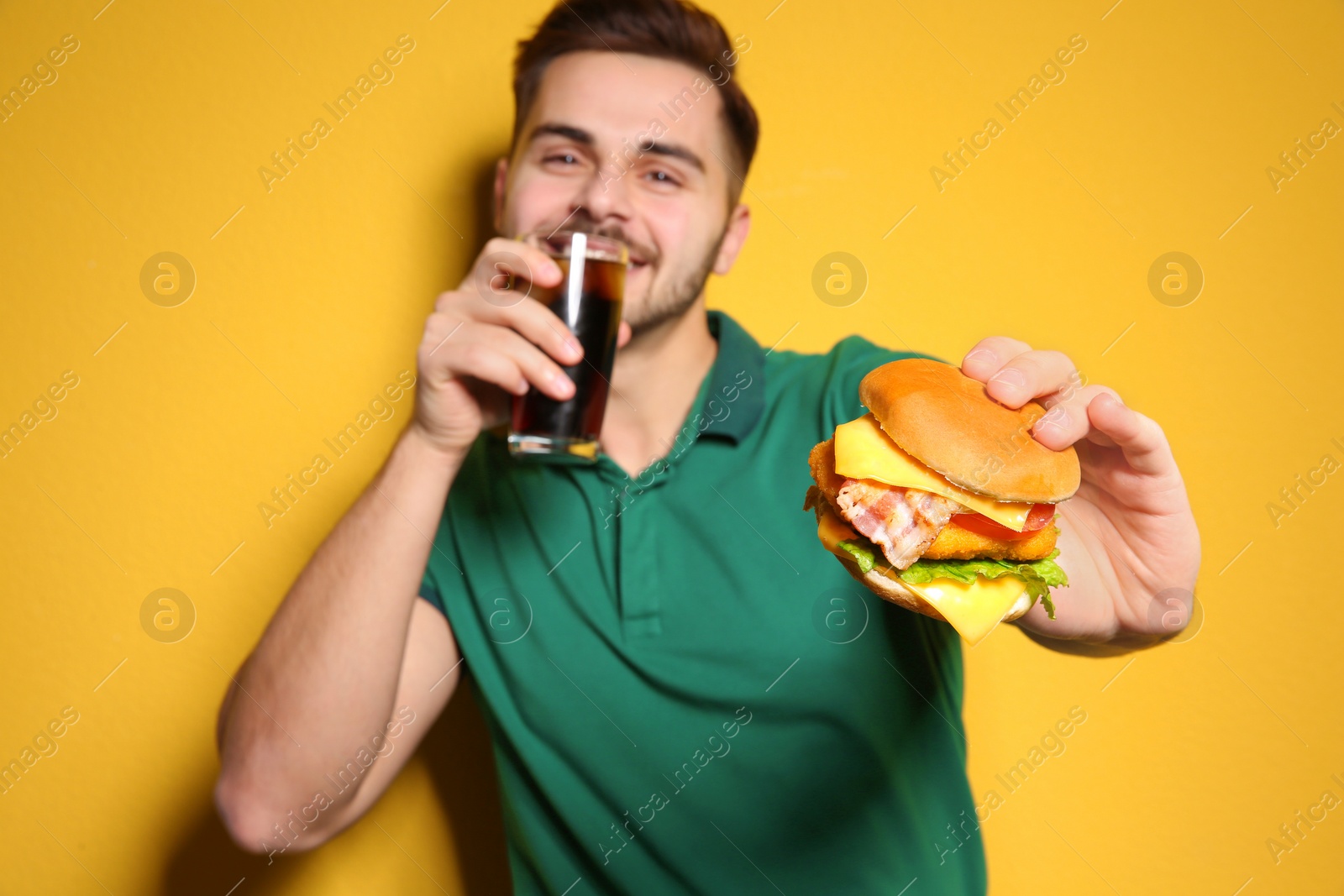 Photo of Handsome man with glass of cola and tasty burger on color background