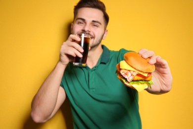 Handsome man with glass of cola and tasty burger on color background