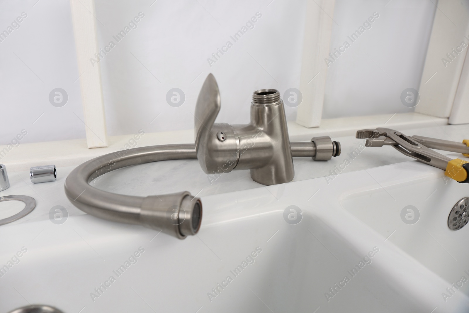 Photo of Disassembled water tap and pipe wrench near sink on countertop