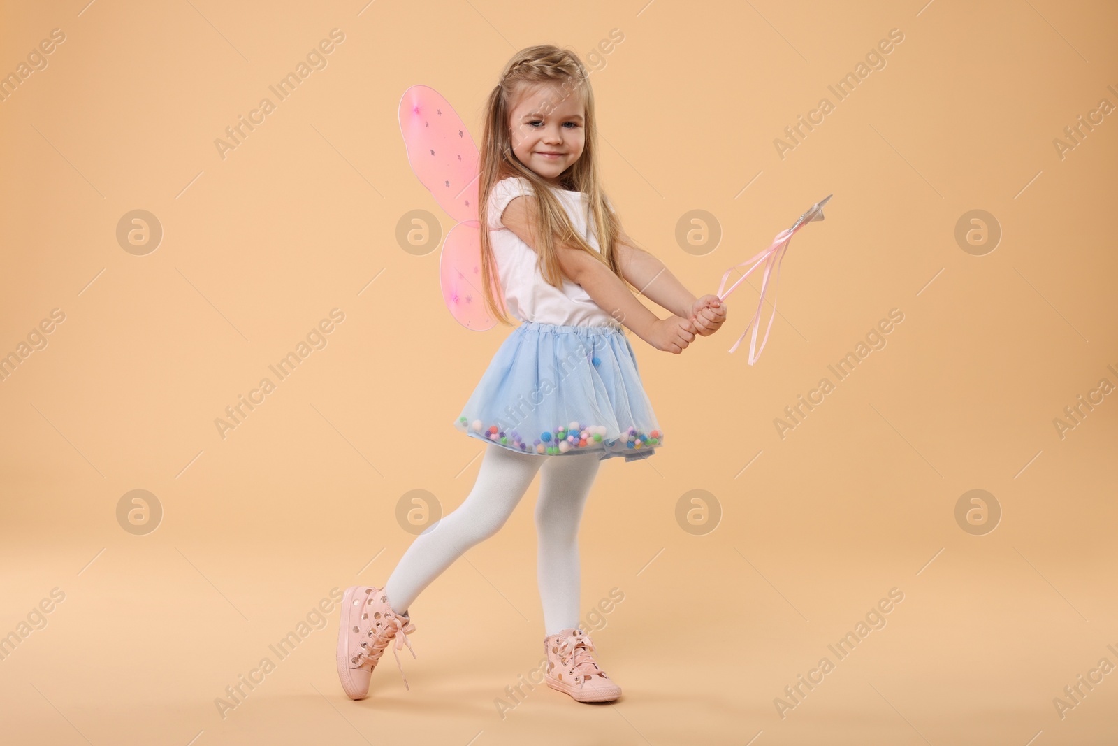 Photo of Cute little girl in fairy costume with pink wings and magic wand on beige background