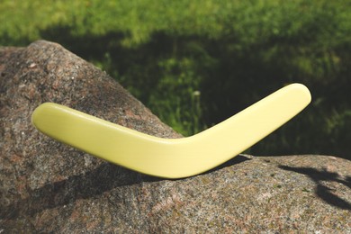 Photo of Sunlit yellow wooden boomerang on stone outdoors
