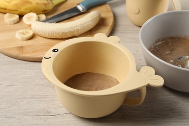 Photo of Baby food. Bowls with banana puree on light wooden table