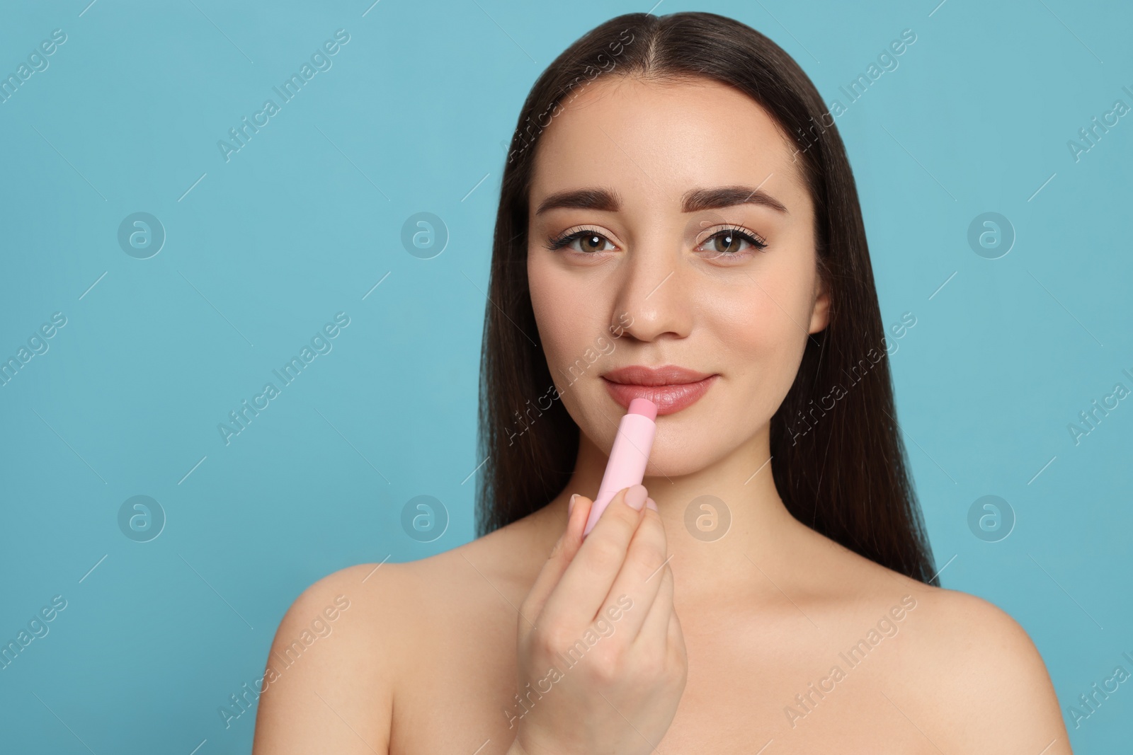 Photo of Young woman applying lip balm on turquoise background, space for text