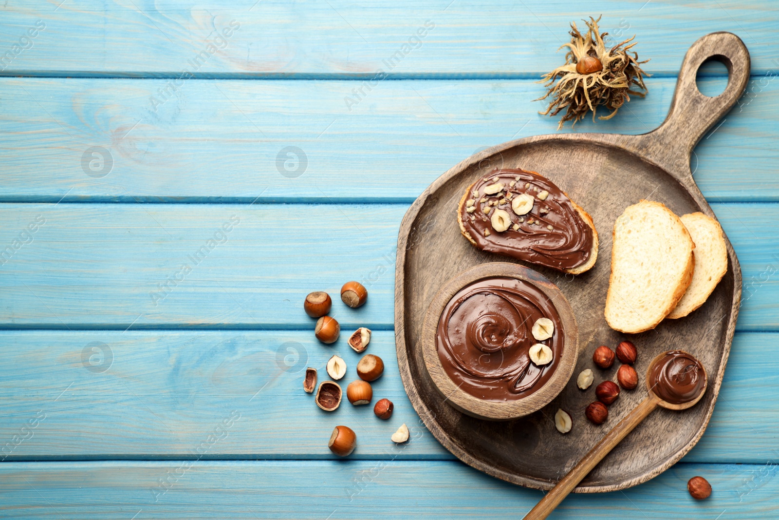 Photo of Flat lay composition with tasty chocolate paste and hazelnuts on light blue wooden table, space for text