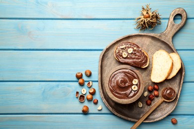 Photo of Flat lay composition with tasty chocolate paste and hazelnuts on light blue wooden table, space for text
