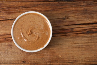 Delicious nut butter in bowl on wooden table, top view. Space for text